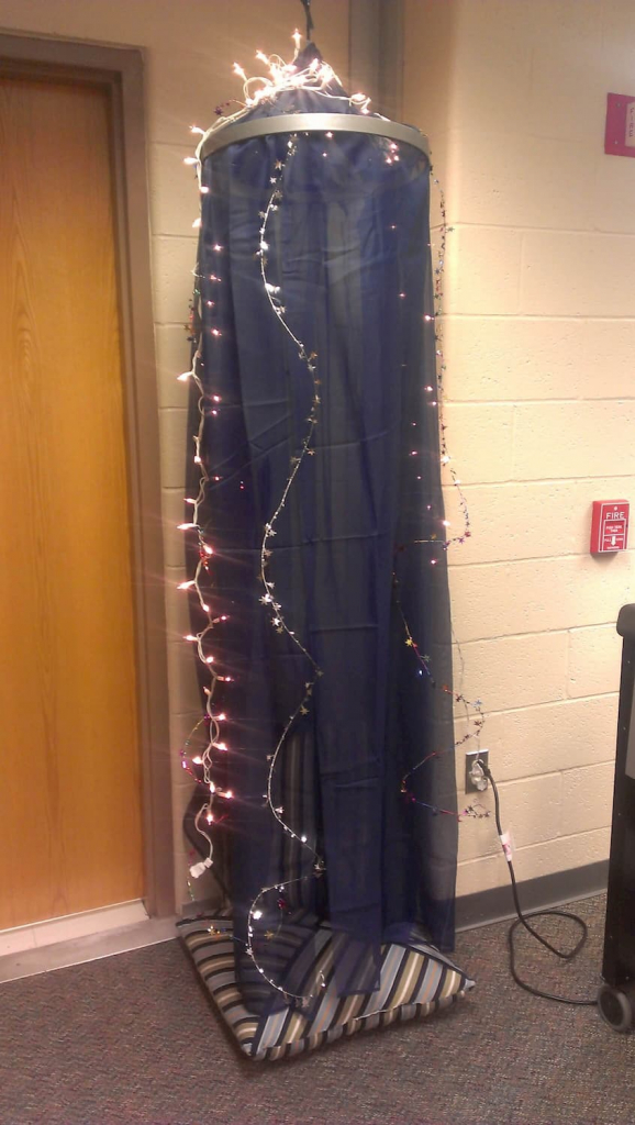 Sheer curtains attached through a hanging hoop to make a do-it-yourself reading tent with string lights wrapped around the top and hanging down.