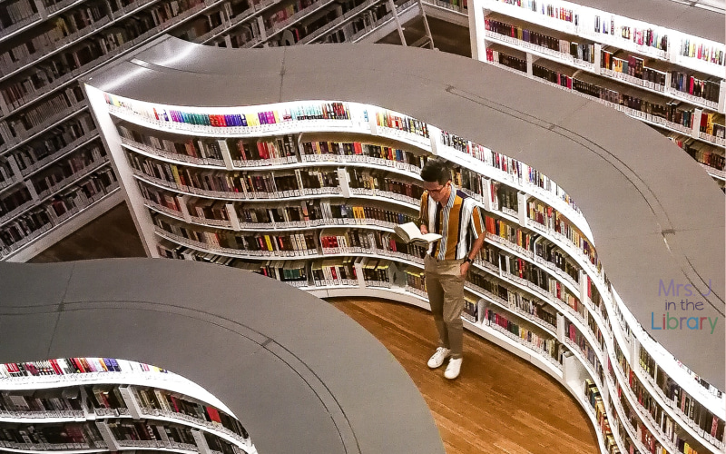 man browsing and reading among curved library shelves.
